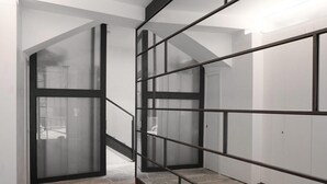Un intérieur moderne avec un escalier, des portes vitrées et une rambarde en métal.