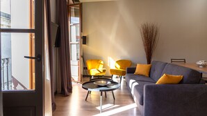 Un salon moderne avec un canapé gris, des fauteuils jaunes, une table basse ronde et une grande fenêtre avec des rideaux.