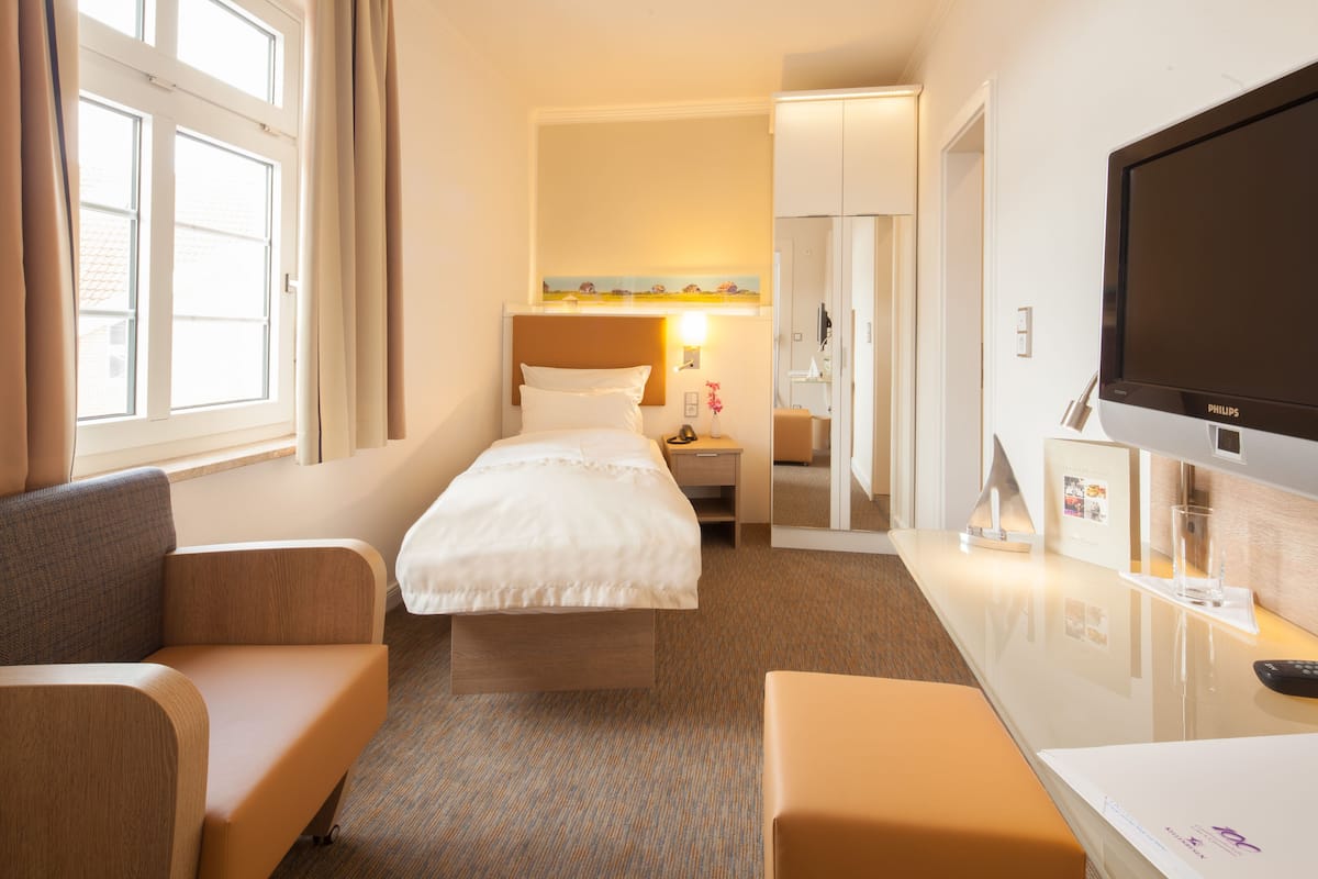 A hotel room with a bed, a sofa, a desk with a TV, and a window with curtains.