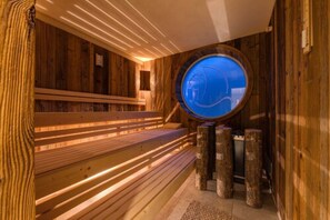 A wooden sauna with benches and a circular window. - Hotel Erholung (Kellenhusen)