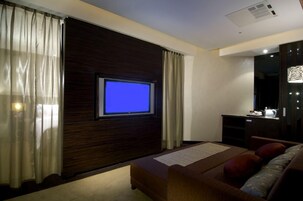 Een hotelkamer met een bed, een tv bevestigd aan een donker houten paneel, een bureau met een lamp en een grote spiegel.