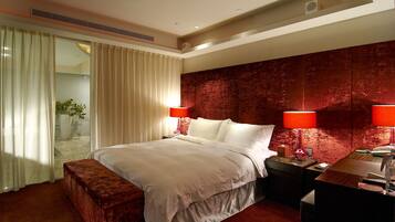A hotel room with a large bed, two bedside lamps, a wooden nightstand, a desk, and a red accent wall.