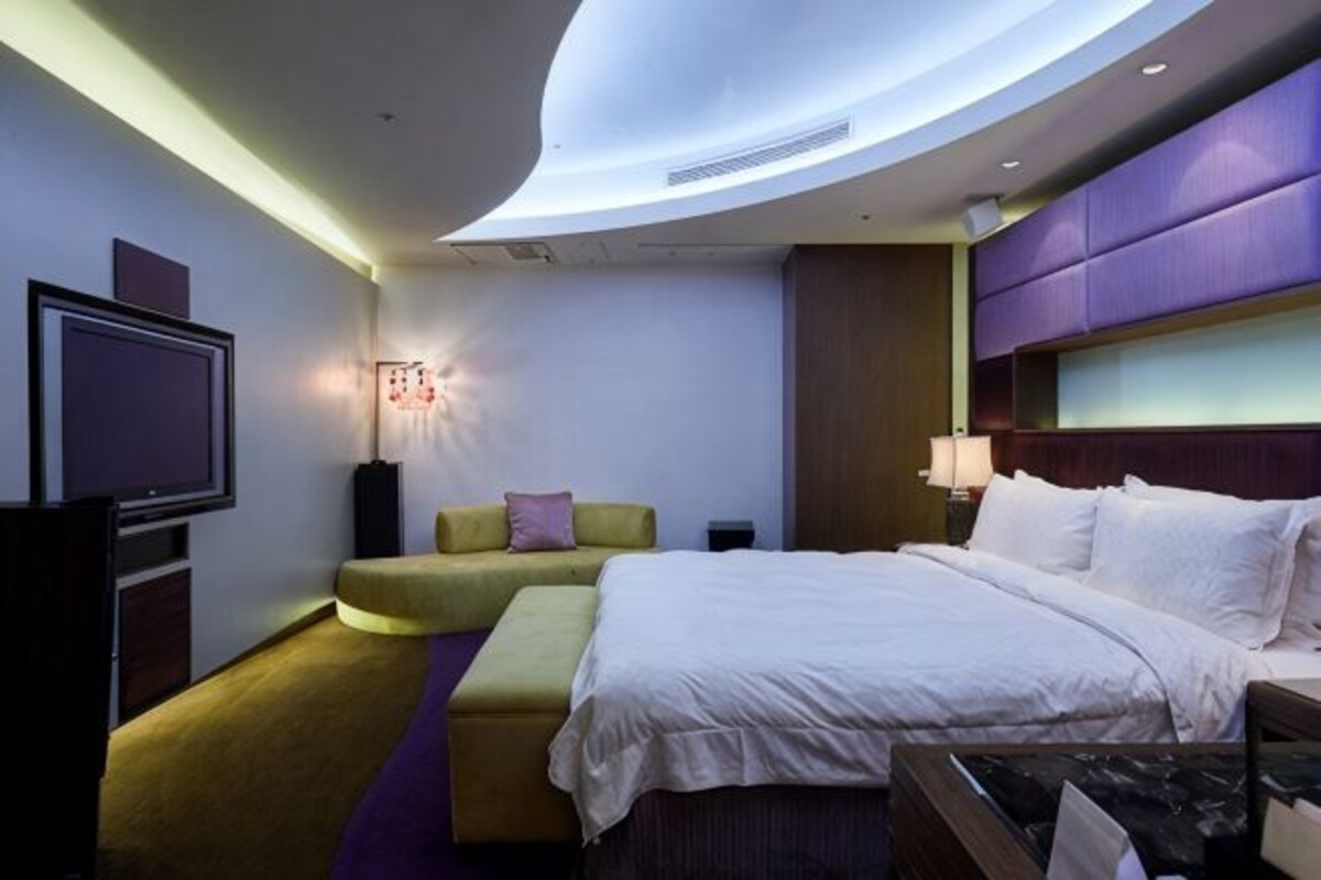 A modern hotel room with a curved ceiling, a large bed, a seating area, and a television.