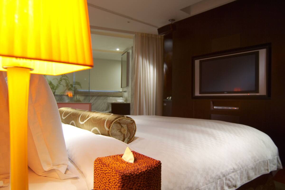 A hotel room with a bed, a bedside lamp, a television, and a mirror.