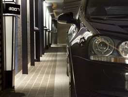 Een auto geparkeerd in een overdekte buitenruimte met betegelde vloer en verticale verlichtingsarmaturen.