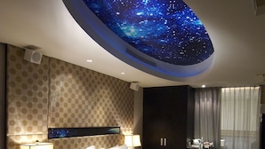 Una habitación de hotel con una cama, un sillón rojo, una mesita de noche, una lámpara, un televisor montado en la pared y un techo con diseño de cielo estrellado.