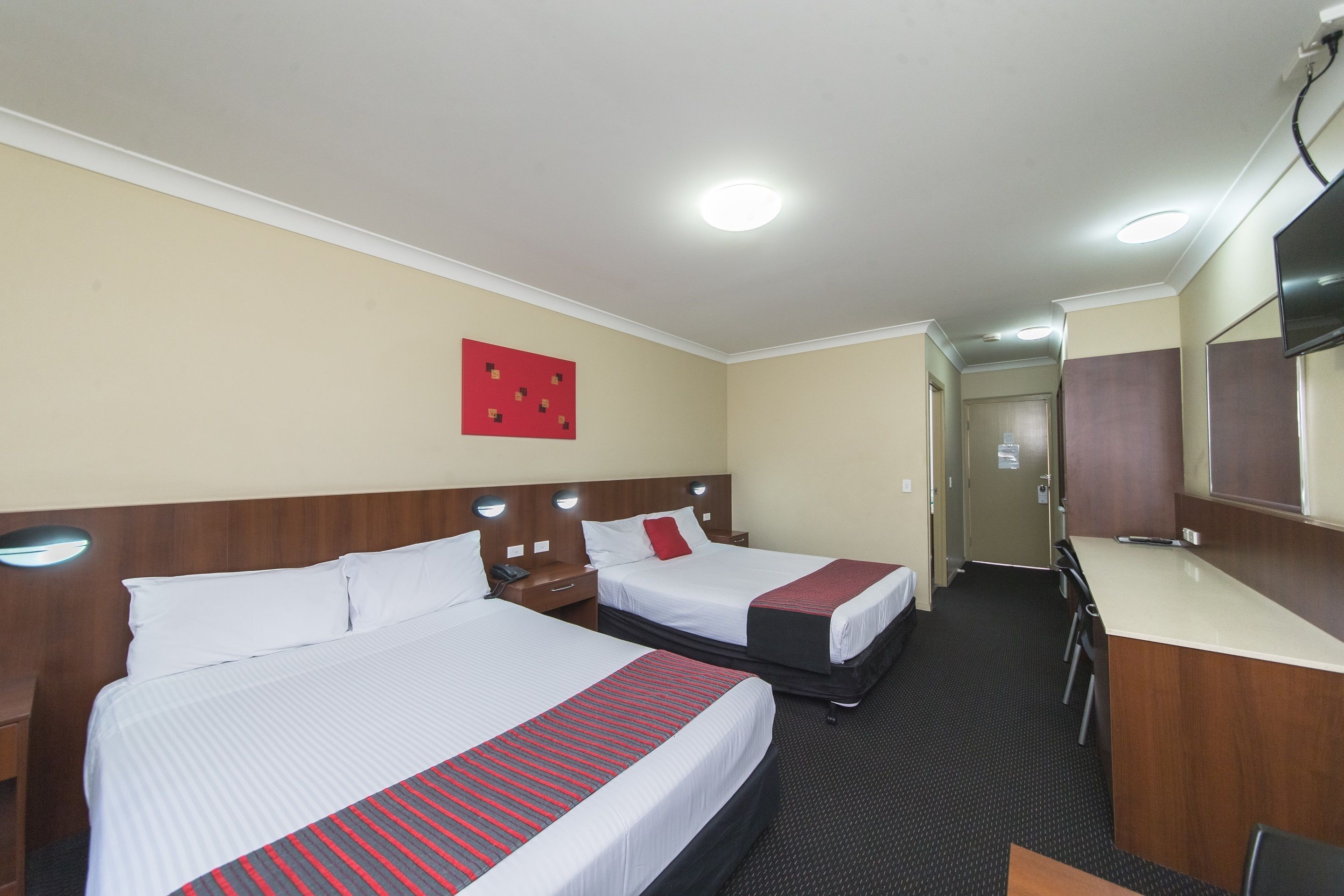 Een hotelkamer met twee bedden, een bureau, een spiegel en een rode wanddecoratie.