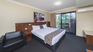Quarto de hotel com uma cama grande, uma mesa, uma cadeira e vista para o verde através de uma porta de correr.