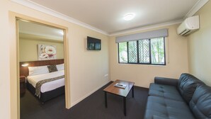 Quarto de hotel com cama, uma pequena mesa, um sofá, uma televisão e uma janela com vista para vegetação.