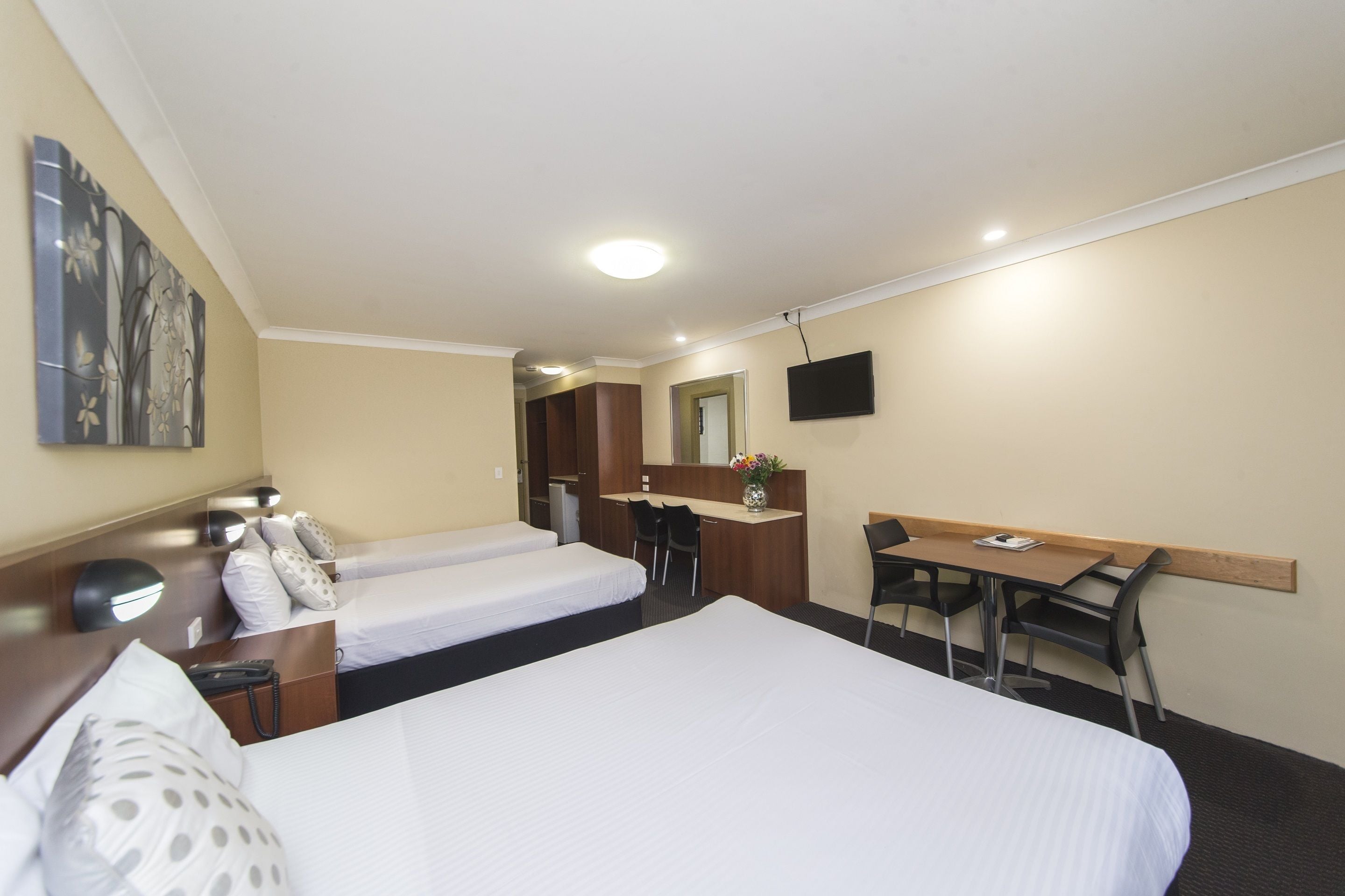 Une chambre d’hôtel avec deux lits simples, un bureau avec une chaise, une petite table, un miroir et un téléviseur fixé au mur.