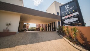 Entrada de hotel com placa indicando quarto disponível, galeria coberta e acesso por caminho de cascalho.