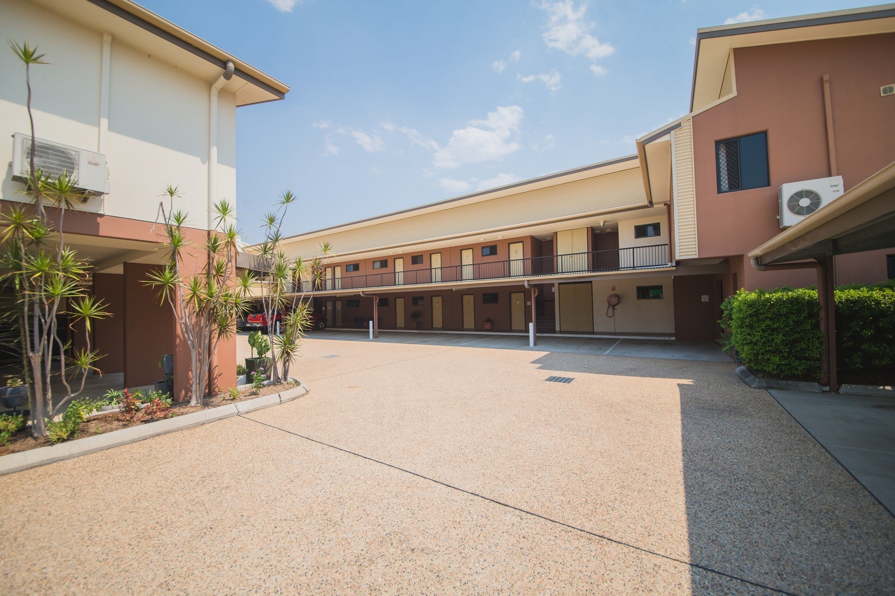A courtyard with a covered walkway, air conditioning units, and potted plants.
