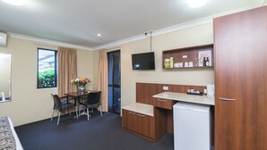 Quarto de hotel compacto com cozinha compacta, área de refeições com mesa e cadeiras, TV fixada na parede e janela com cortinas.