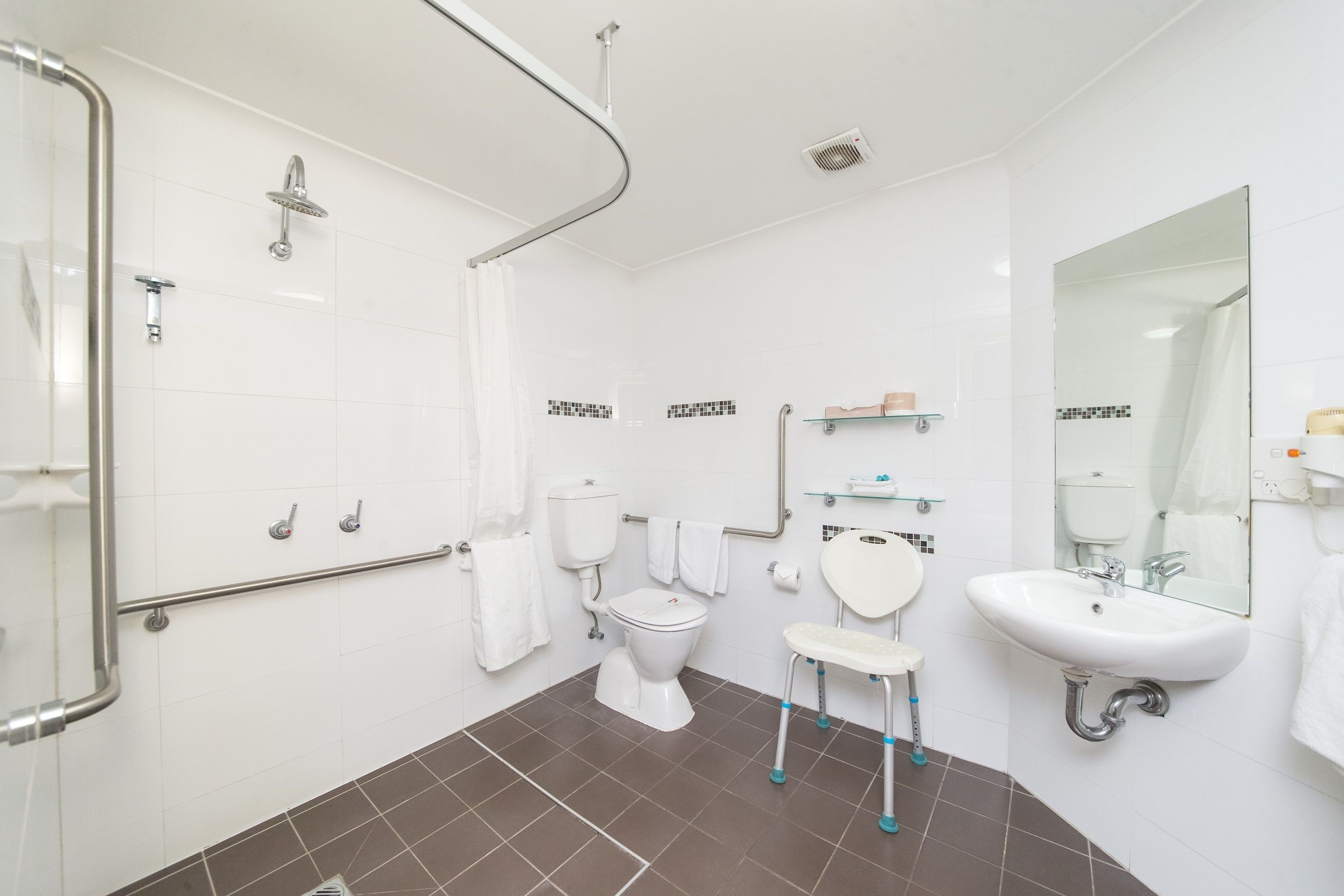 A modern bathroom with a shower, toilet, and sink, equipped with grab bars and a wheelchair-accessible bench.