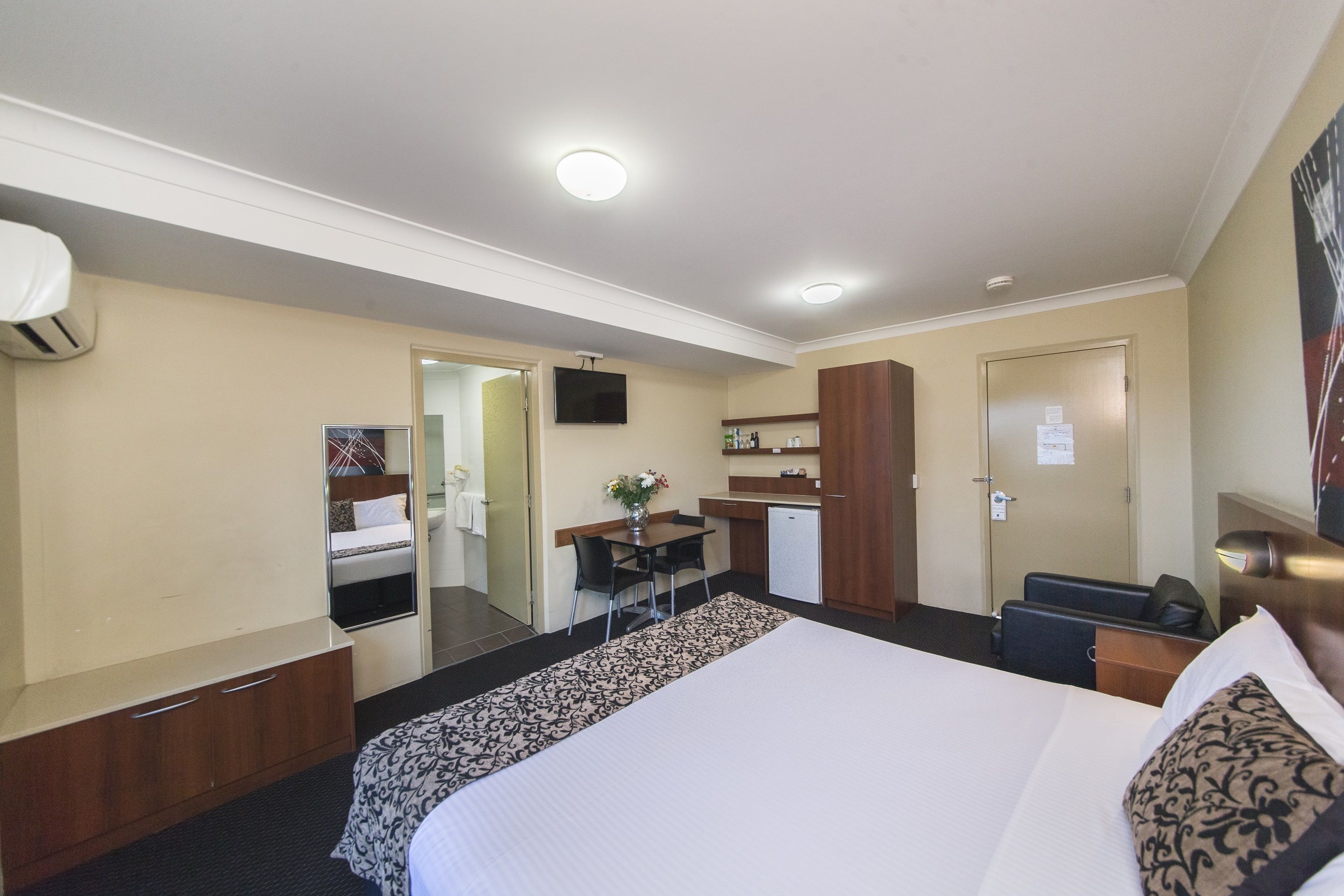 A hotel room with a bed, a desk, a chair, a small kitchenette, and a TV.