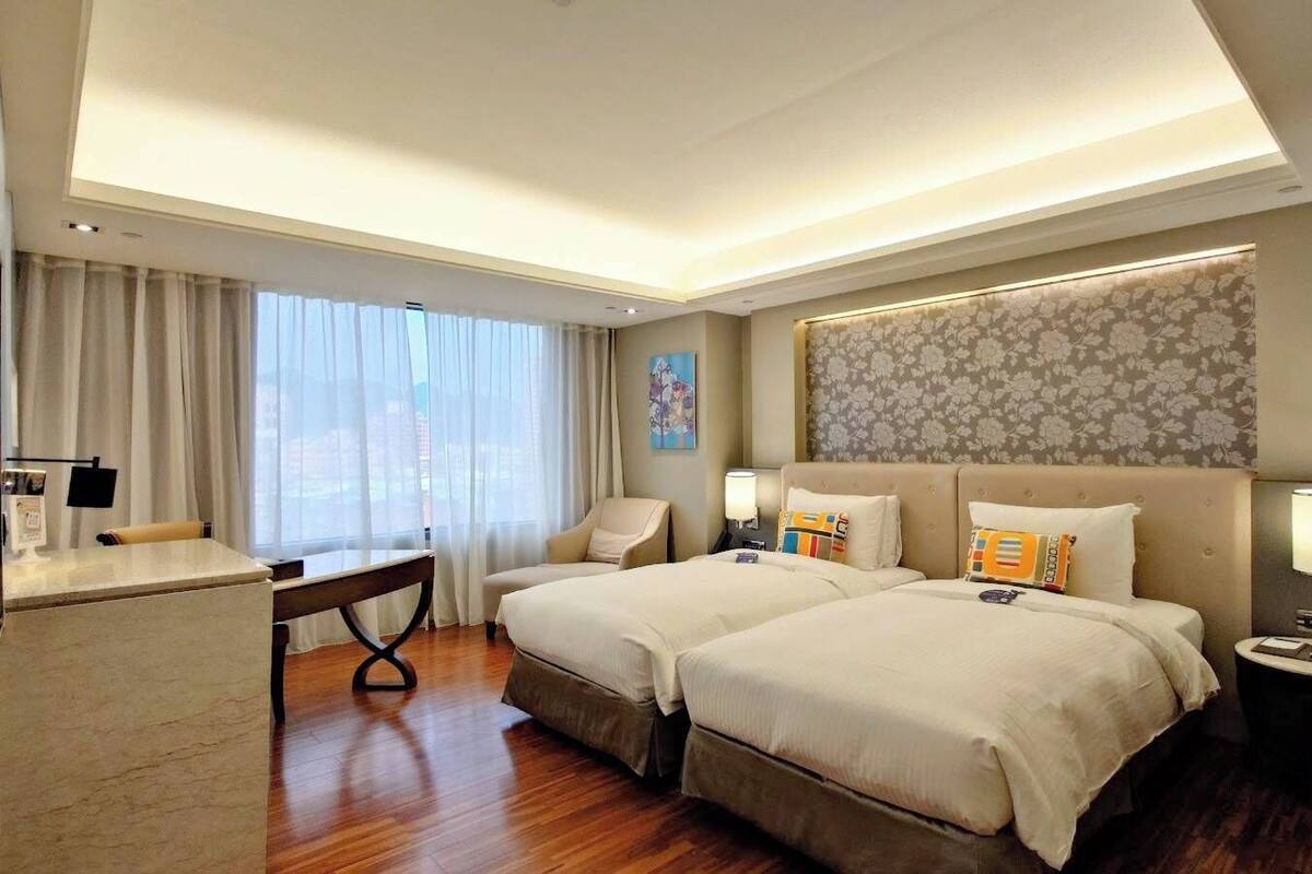 Ein Hotelzimmer mit zwei Betten, einem Schreibtisch, einem Stuhl, einer Schreibtischlampe und einer Wandleuchte.