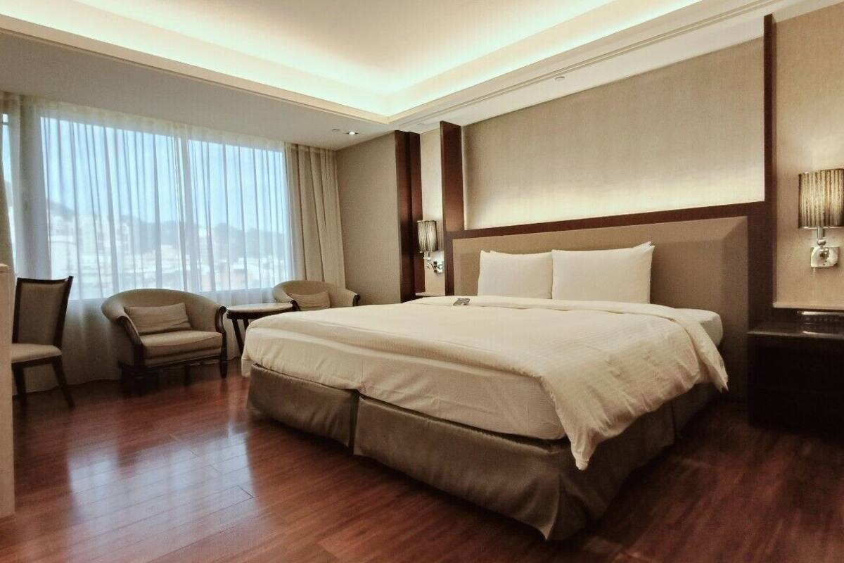 Ein Hotelzimmer mit einem großen Bett, einem Schreibtisch, einem Stuhl und Blick auf die Stadt durch das Fenster.