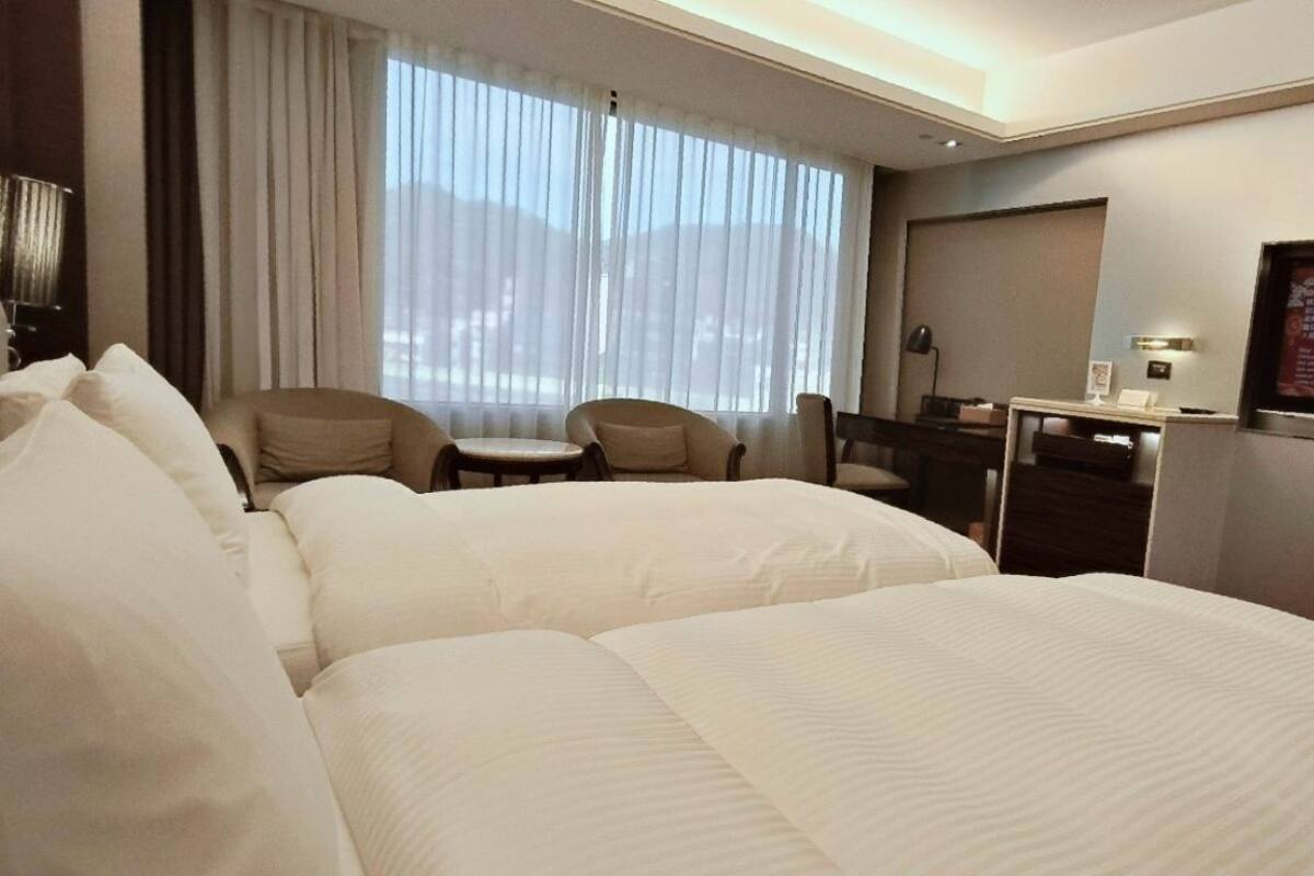 Ein Hotelzimmer mit zwei Betten, einem Schreibtisch, einem Stuhl und einem Fernseher an der Wand.