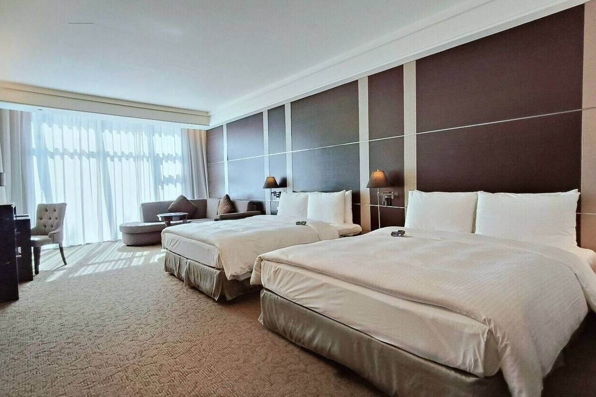 Ein Hotelzimmer mit zwei Betten, einem Sofa, einem Schreibtisch und einem großen Fenster mit Vorhängen.