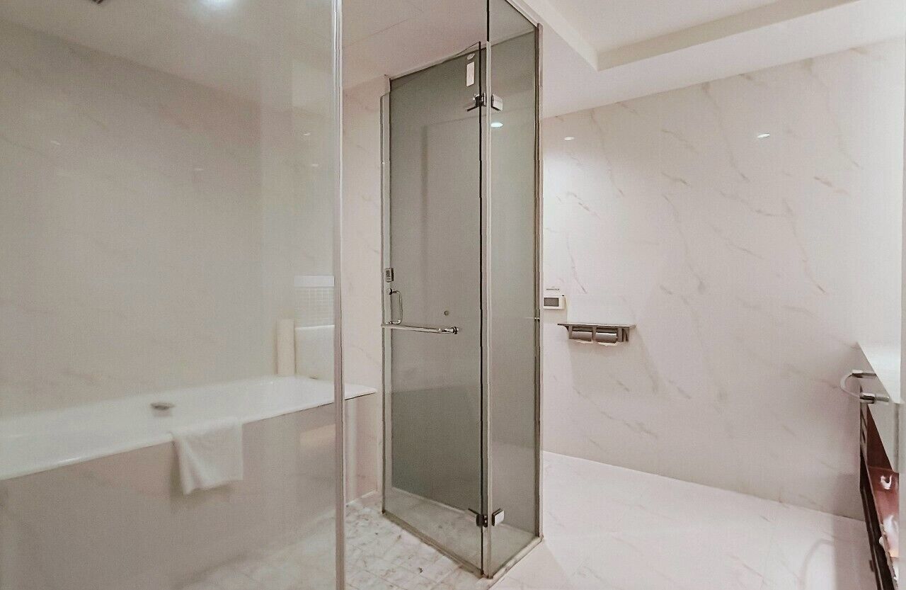 A modern bathroom with a glass-enclosed shower, a white marble wall, and a white bathtub.