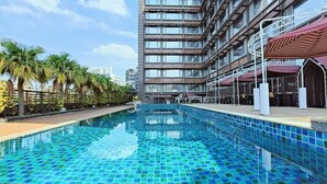 Un hotel moderno con piscina en la azotea, palmeras y vistas al horizonte de la ciudad.