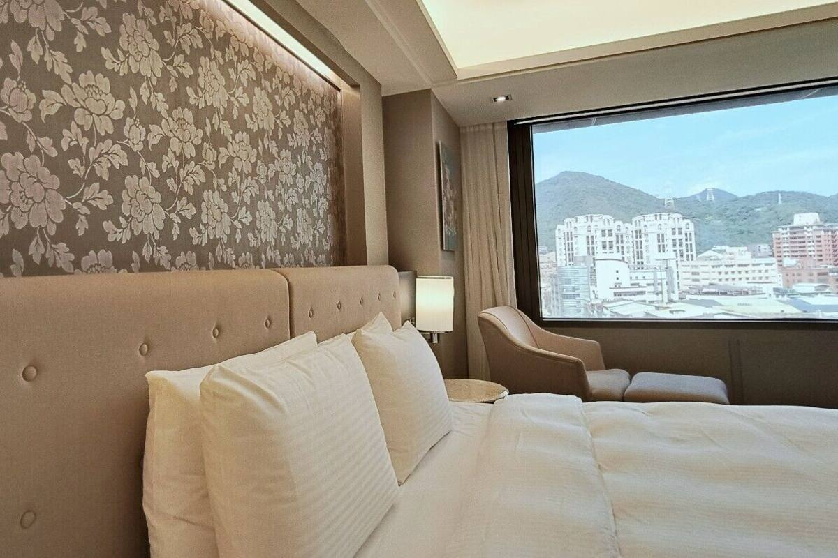 Ein Hotelzimmer mit einem großen Bett, einem Sofa, einem Sessel und einem Fenster mit Blick auf die Stadt.