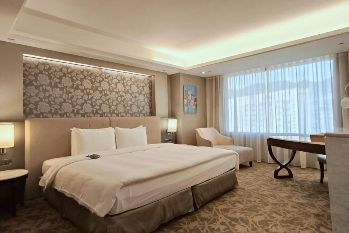 Ein Hotelzimmer mit einem großen Bett, einem Schreibtisch, einem Stuhl und einem fenster mit Vorhängen.