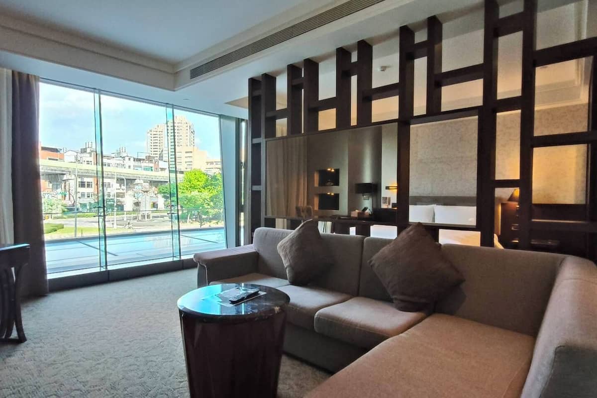 Ein modernes Hotelzimmer mit großem Fenster und Blick auf die Stadt, einer Couch, einem Couchtisch und einer Wand in dunklem Holz.