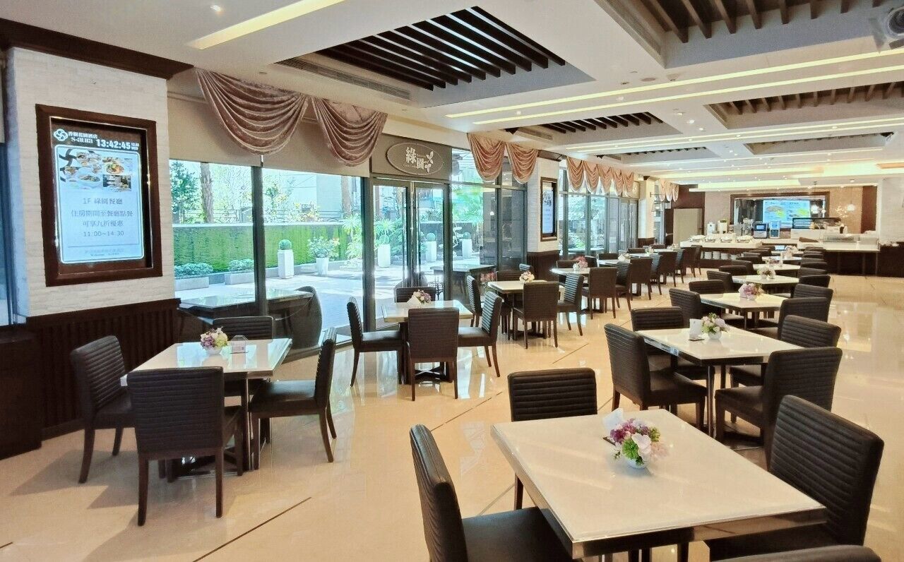 Um restaurante espaçoso com várias mesas e cadeiras, grandes janelas e decoração moderna.