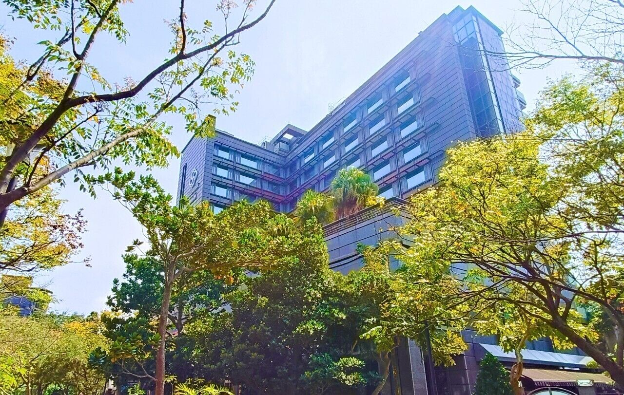 A modern building with a glass facade and multiple floors, surrounded by trees.