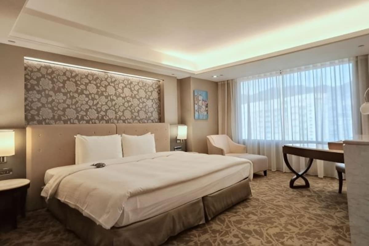 Habitación de hotel con una cama grande, un escritorio, una silla y una ventana con cortinas.