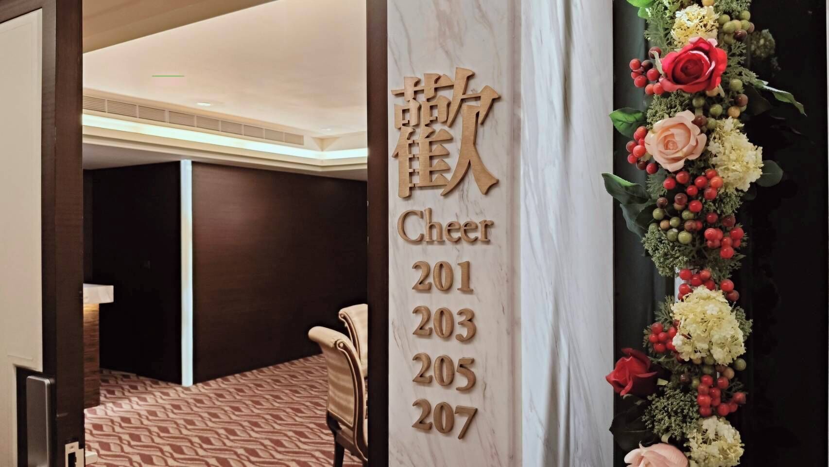 A hotel room with a wooden number sign, a floral decoration, and a patterned carpet.