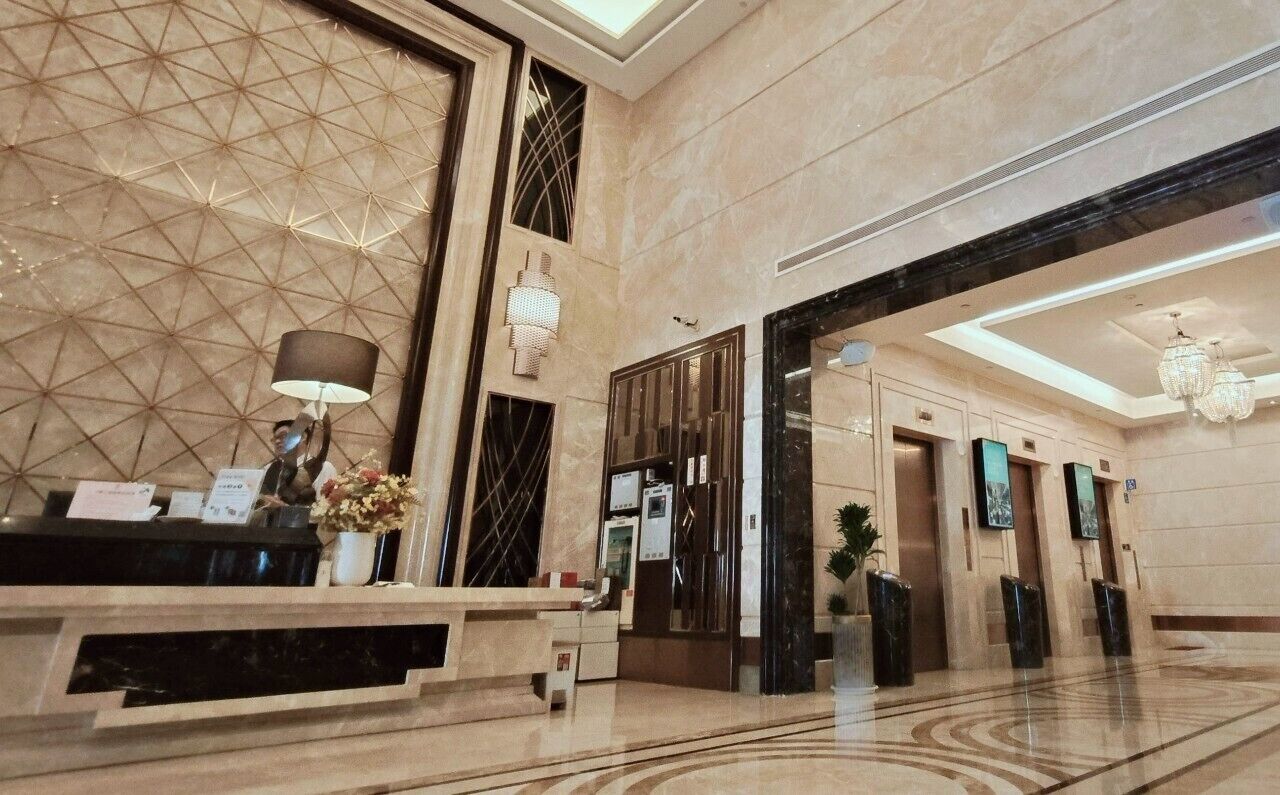 A modern lobby with a reception desk, a geometric patterned wall, and a chandelier.