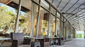 Un espacio exterior con asientos de mimbre, mesas, ventanas amplias y un paseo techado.