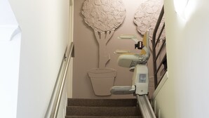 Un escalier avec une rampe, des marches recouvertes de moquette et un fauteuil dentaire fixé au mur.