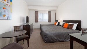 Une chambre d’hôtel avec deux lits, un bureau, une chaise, une télévision et un tableau au mur.