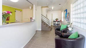 Un espace d’accueil comprenant un comptoir, un escalier et un coin salon avec des coussins verts.