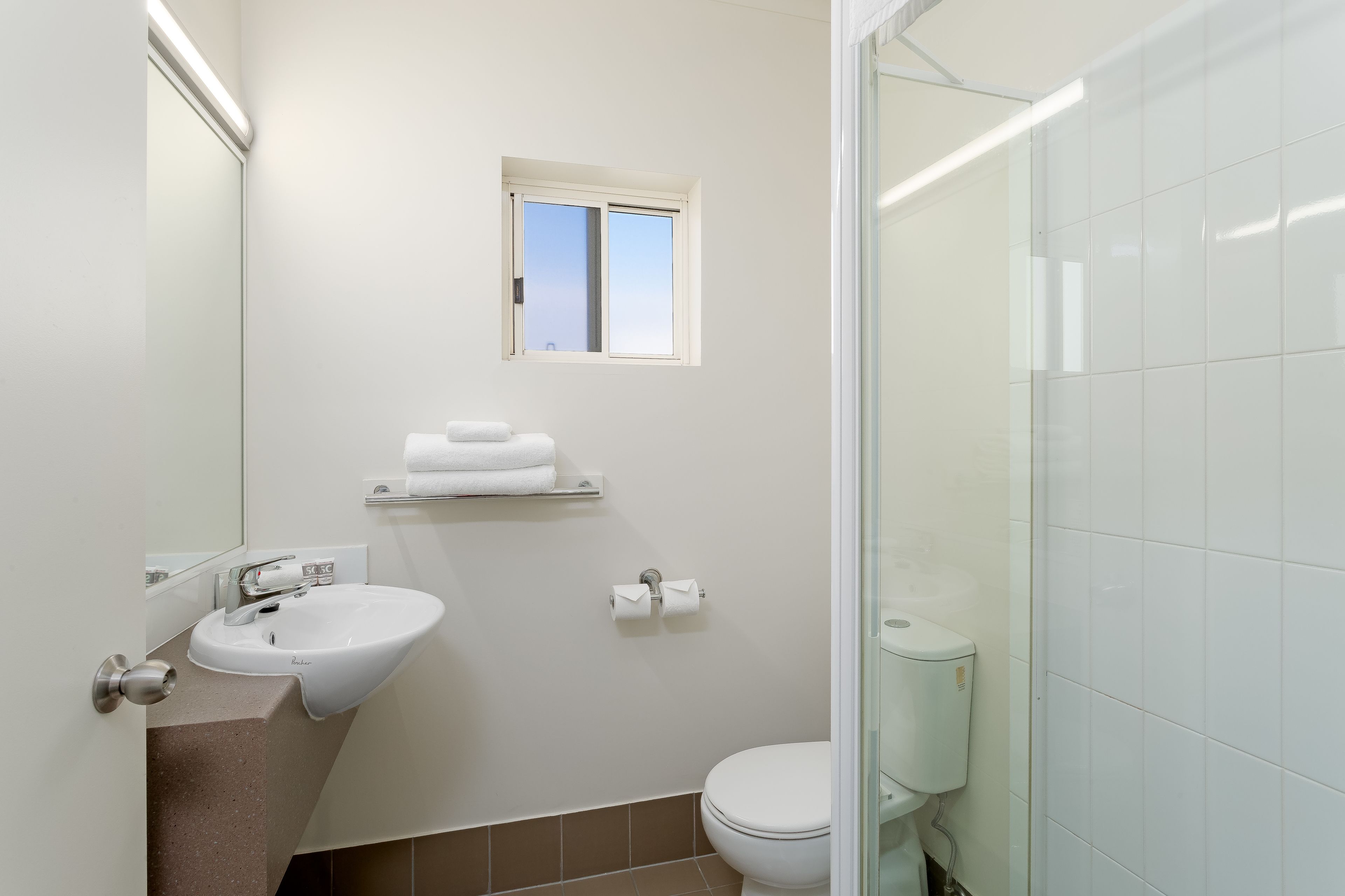 Une salle de bain moderne avec un lavabo blanc, des toilettes et une petite fenêtre.