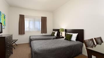 A hotel room with two beds, a desk, a chair, a dresser, and a window with curtains.
