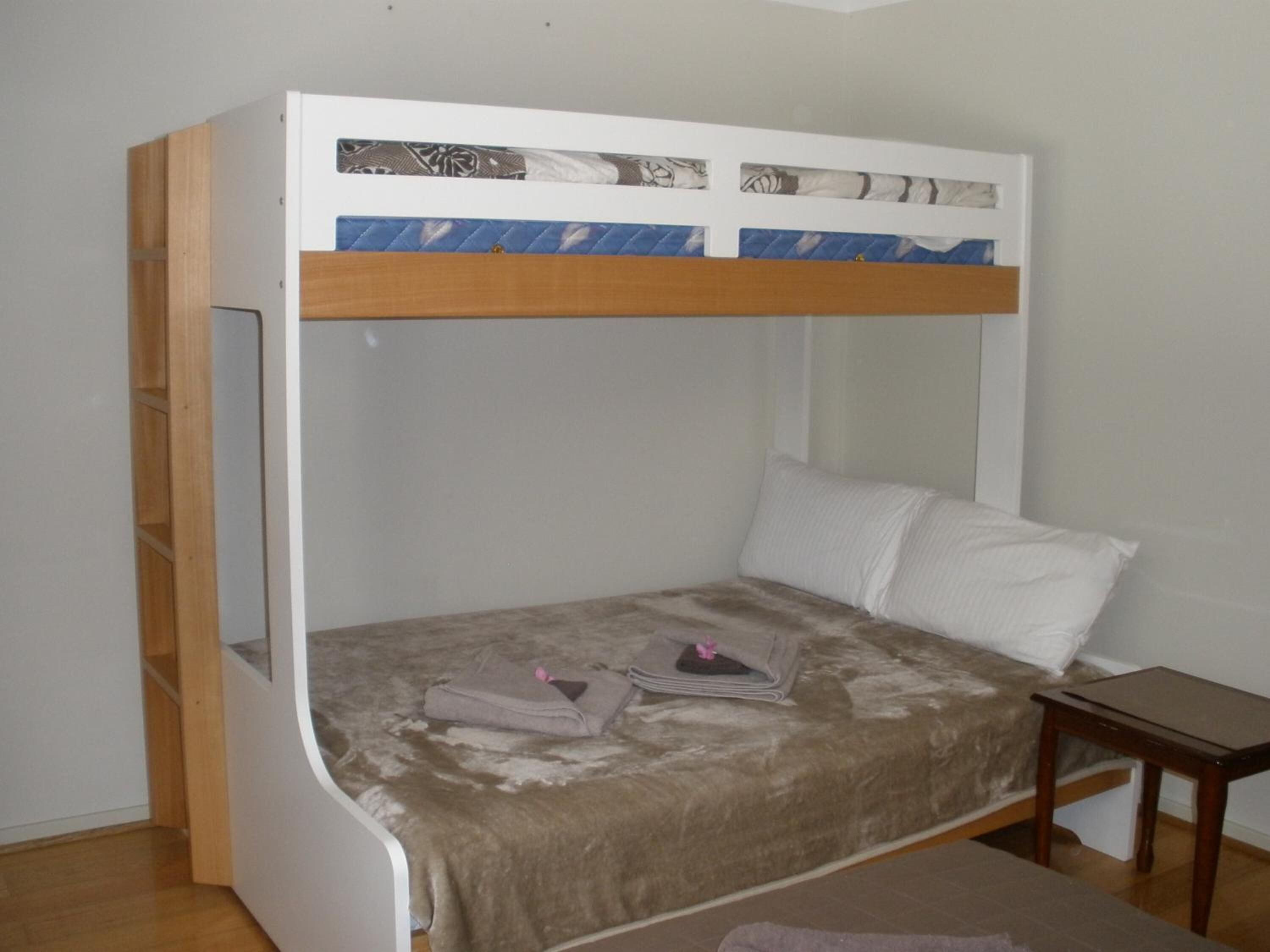 A bunk bed with a wooden frame and a headboard with a decorative panel. There is a small bedside table and a pillow on the bed.