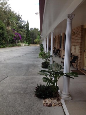 A building with a covered outdoor seating area, columns, and potted plants. - Palms Oasis Motel (Coopernook)