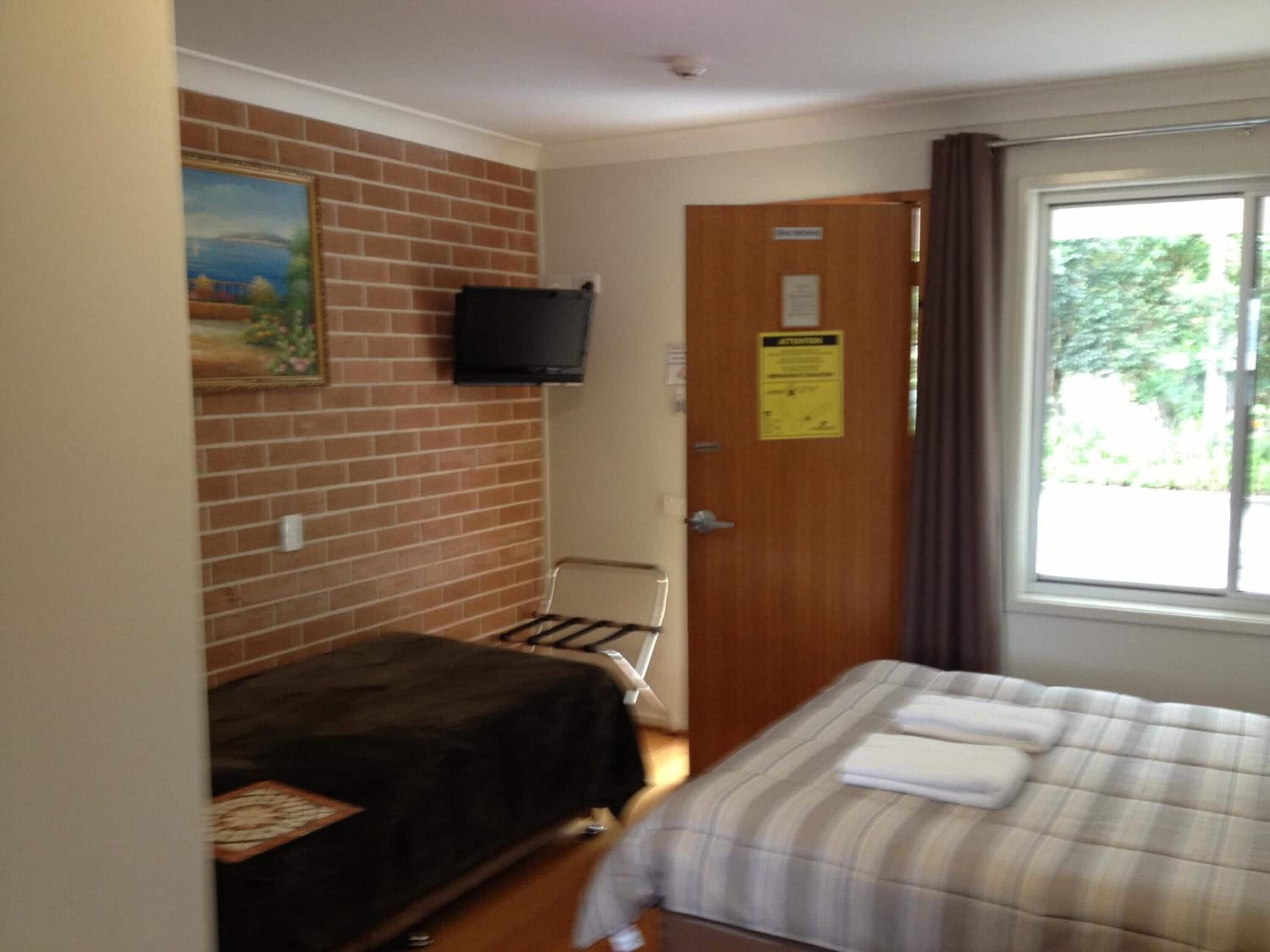 A room with two beds, a TV on the wall, and a window with curtains.