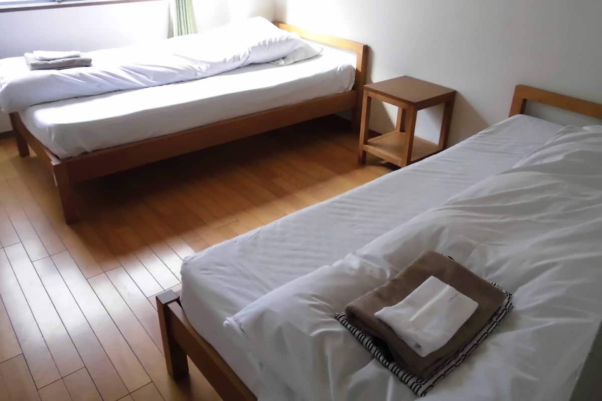A room with two single beds, wooden flooring, and a small bedside table.