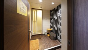 A hotel room with a wooden door, a sign indicating a shower room, a small round table, a trash bin, and a patterned wall. - Hotel Taiyo (Osaka)