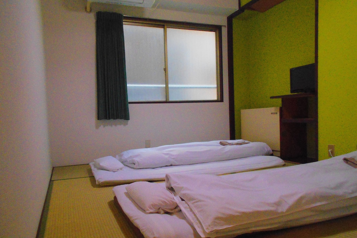 A room with two beds, a window with a curtain, and a green wall.