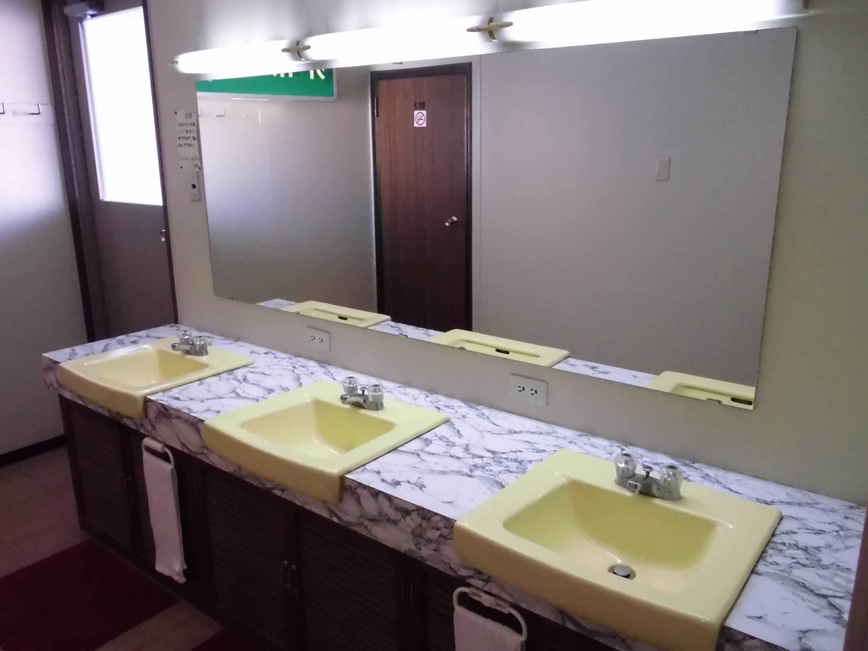 A restroom with three sinks, a large mirror, and a green exit sign.