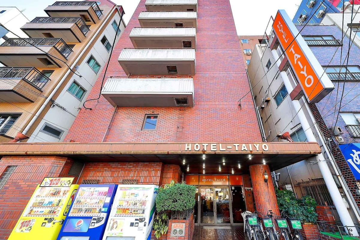 Um hotel com uma placa chamativa, uma máquina de vendas automática e uma área de estacionamento para bicicletas.