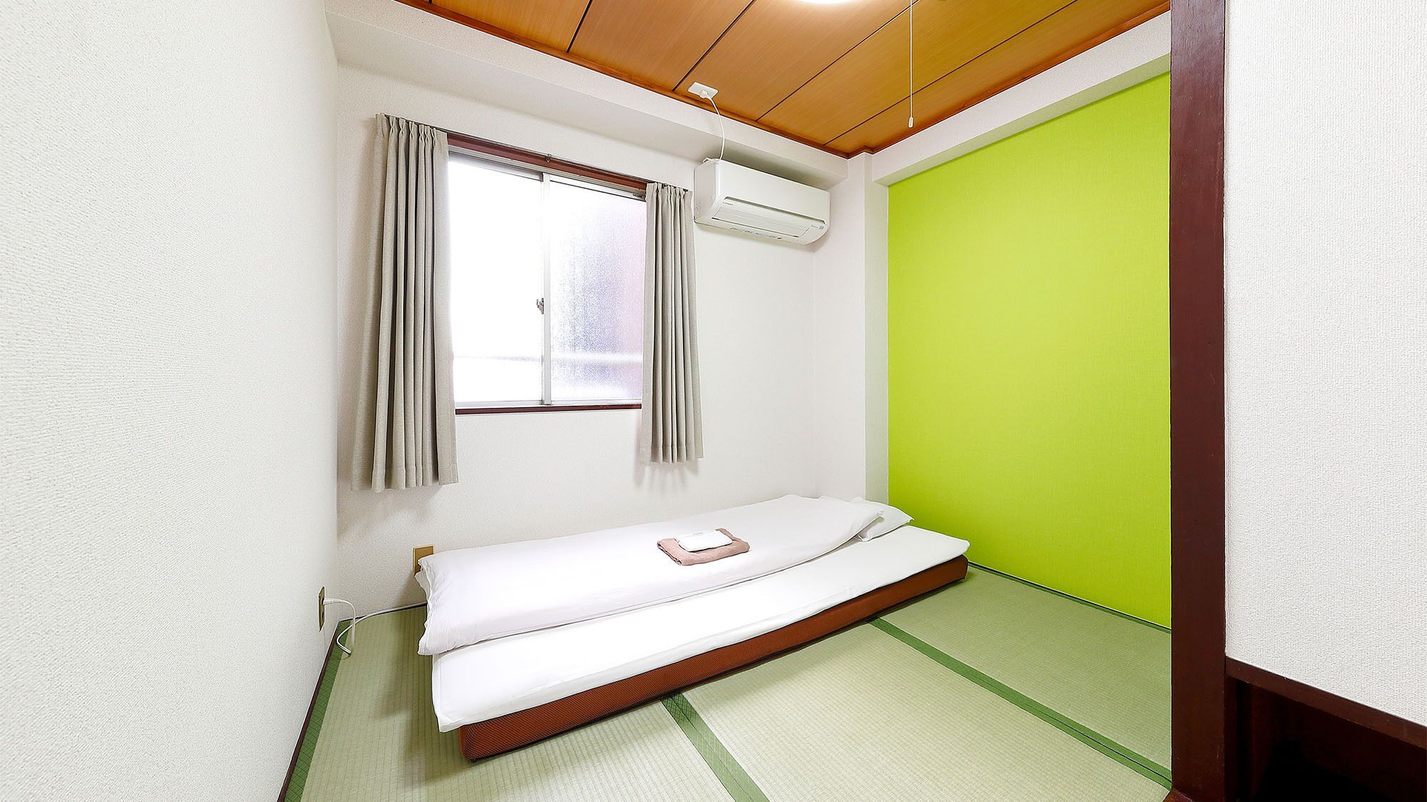 A small room with a bed, a window with curtains, an air conditioning unit, and a green wall.