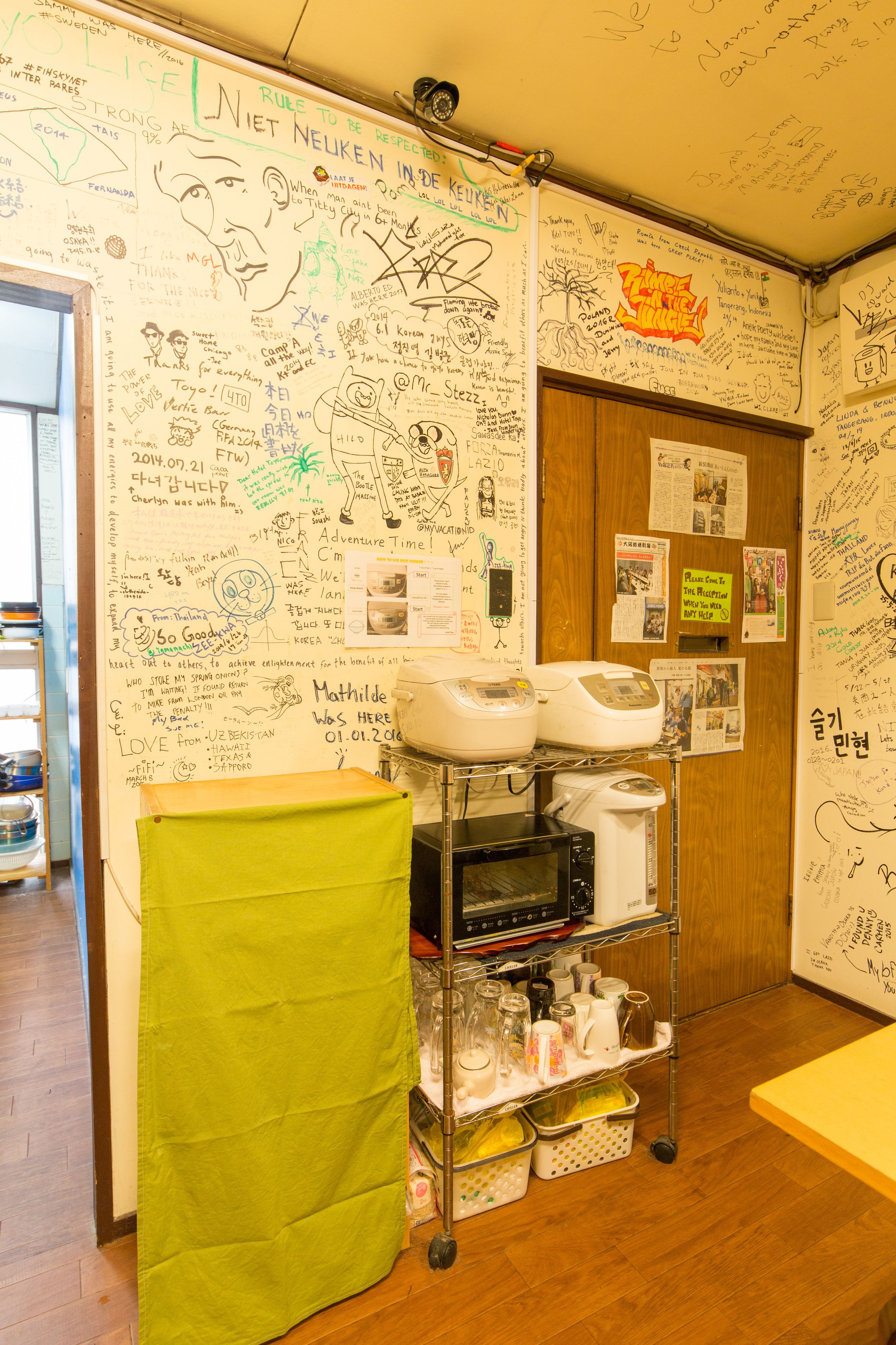 A room with a whiteboard covered in various writings and drawings, a green towel hanging on a rack, and a cart with kitchen appliances.