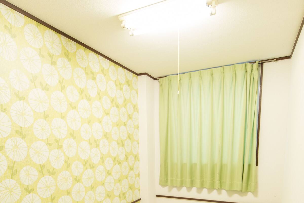 Une pièce avec un lit, une fenêtre ornée de rideaux verts et un papier peint à motifs.